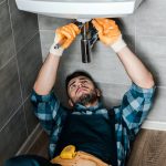 bearded repairman fixing water damage with adjustable wrench in bathroom
